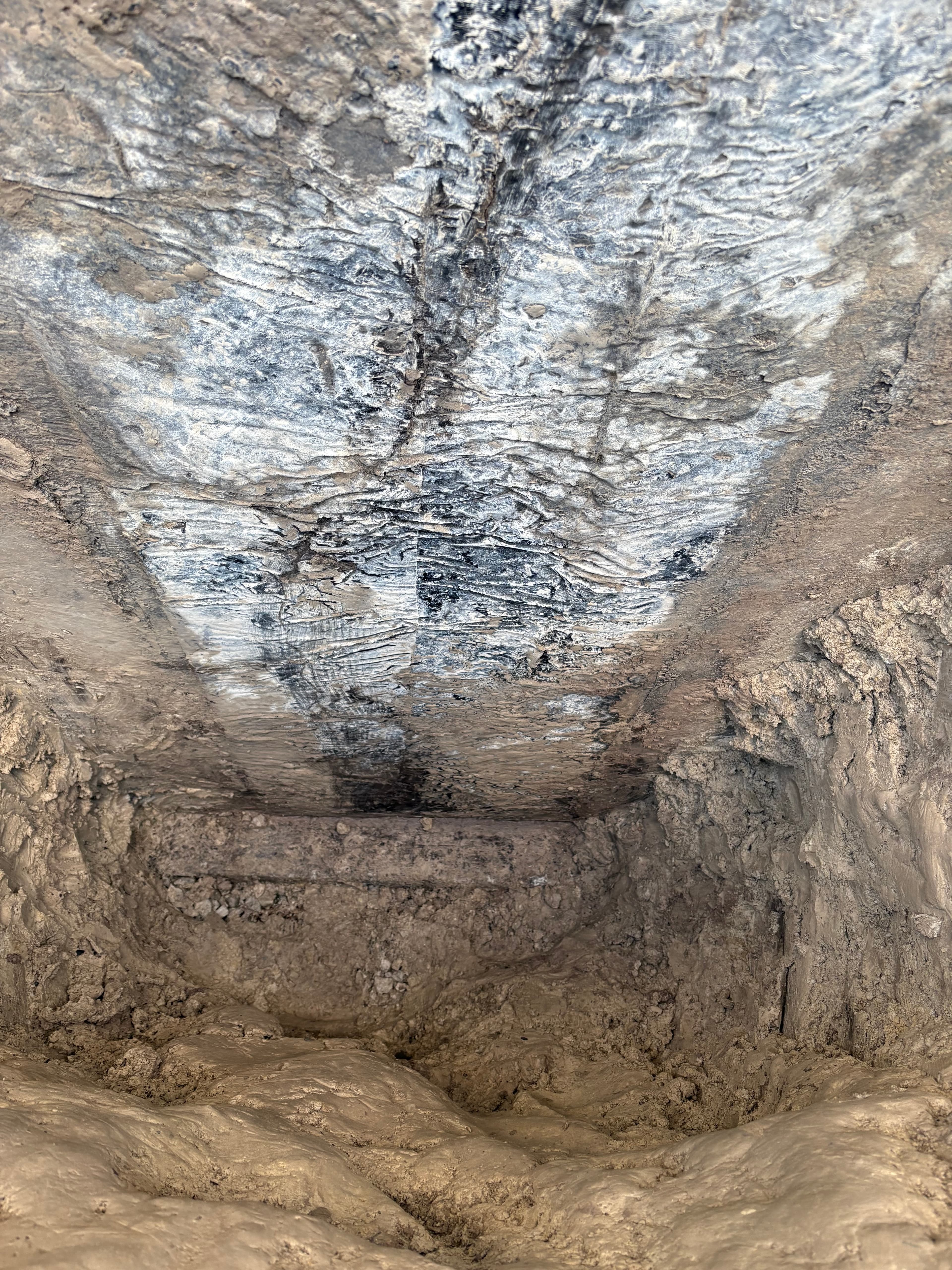 Rough, textured wall in a narrow excavation featuring a dark horizontal stripe across it.
